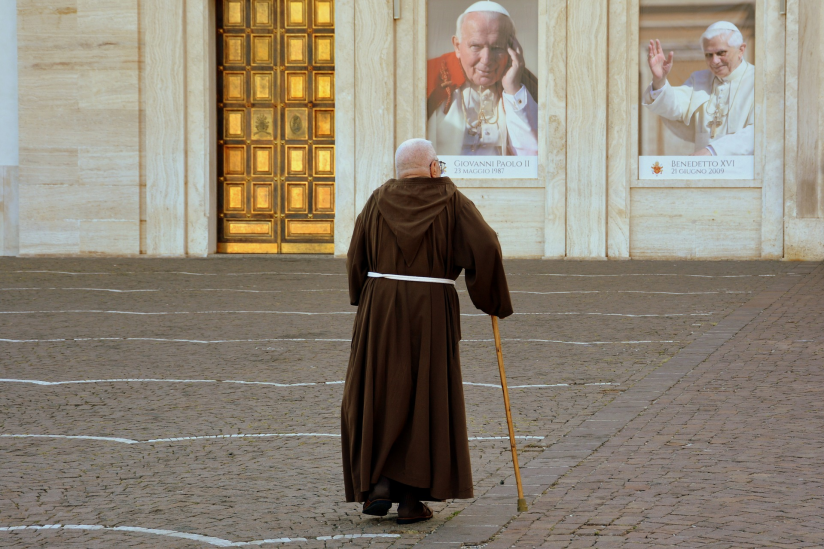 Ein Mönch vor den Bildern zweier Päpste.