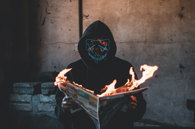Ein vermummter Mensch liest eine brennende Zeitung