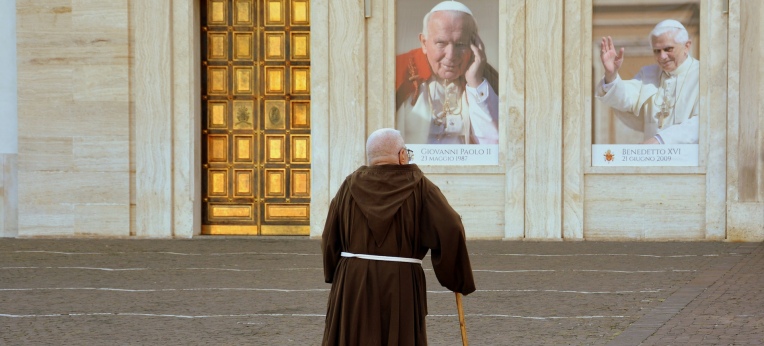 Ein Mönch vor den Bildern zweier Päpste.
