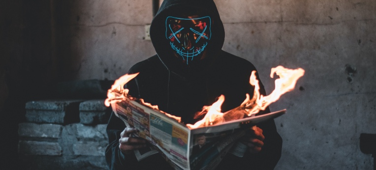 Ein vermummter Mensch liest eine brennende Zeitung
