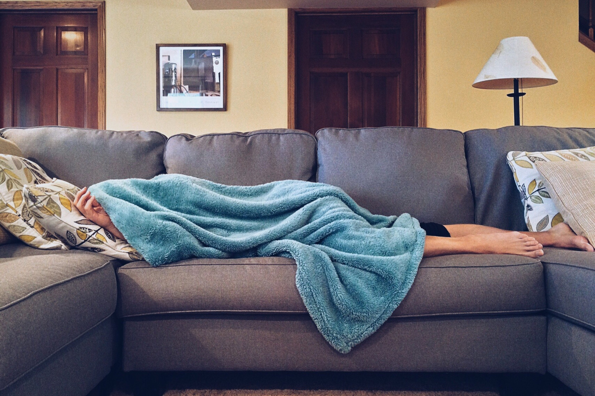 Frau liegt unter einer Decke auf dem Sofa